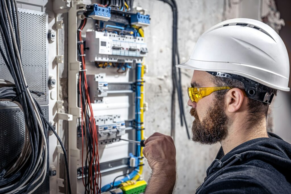 A male electrician works in a switchboard with an electrical connecting cable.