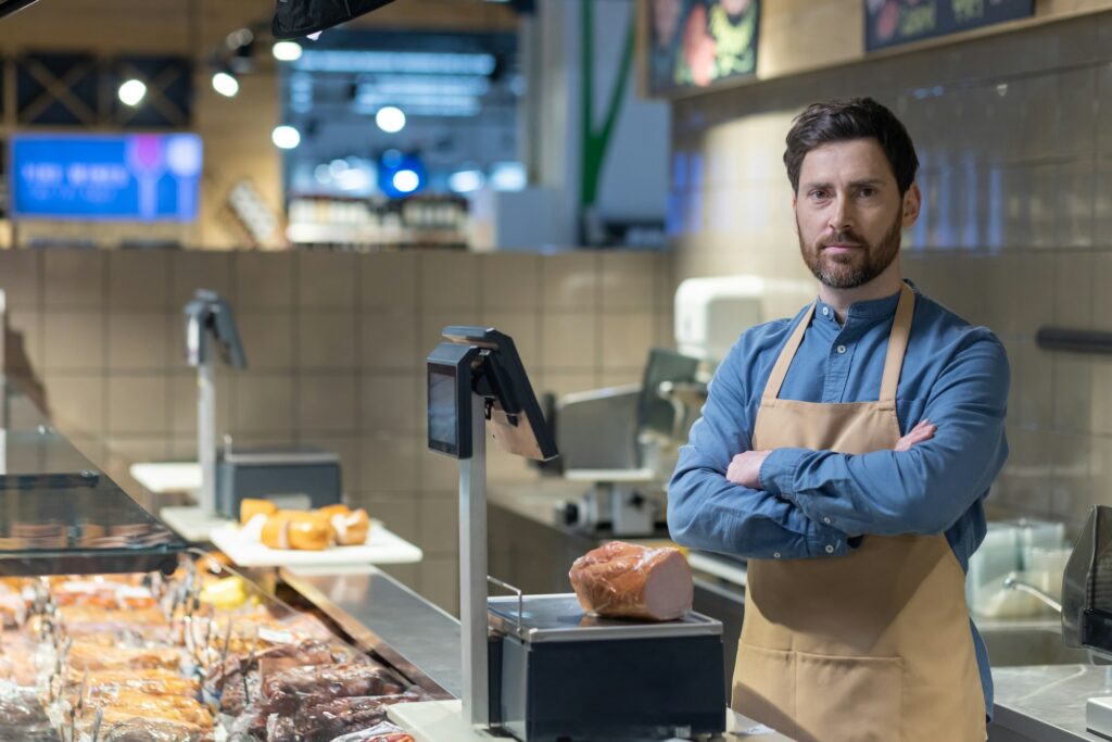 Confident butcher standing behind counter in modern grocery store with fresh meat display